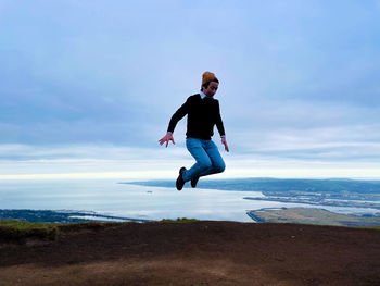 Full length of young man jumping against sky