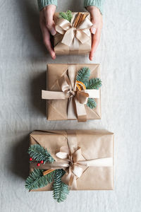 Women's hands hold a beautifully wrapped christmas present, decorated with natural decor and ribbon.