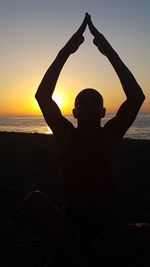 Silhouette man sitting on beach against sky during sunset