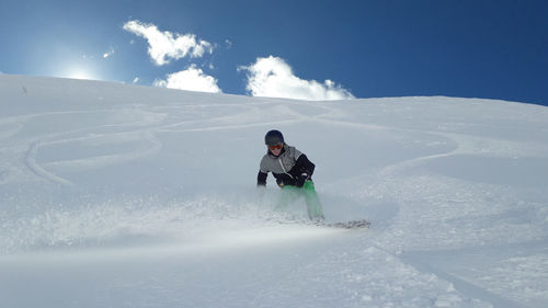 Young man snowboarding on snowcapped mountain against cloudy sky