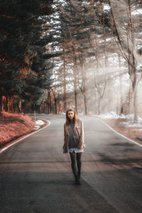 Portrait of young woman standing on road amidst trees