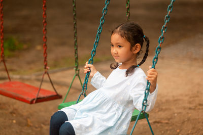 Thoughtful girl on swing at playground