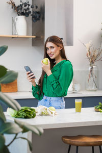 An attractive brunette woman holds a green apple and smiles at the camera. healthy lifestyle