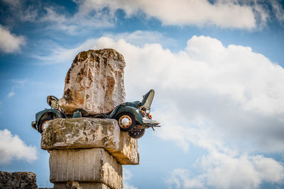 Low angle view of car crushed under rocks against cloudy sky