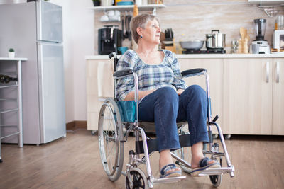 Full length of woman sitting on wheelchair at kitchen