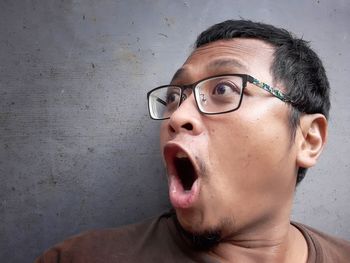 Close-up portrait of man wearing eyeglasses against wall