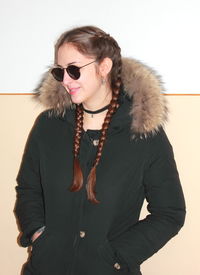 Portrait of young woman wearing sunglasses standing against white background