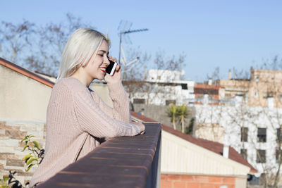 Smiling woman talking on mobile phone against sky