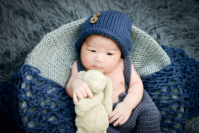 High angle view of cute baby boy lying down in basket with stuffed toy on rug