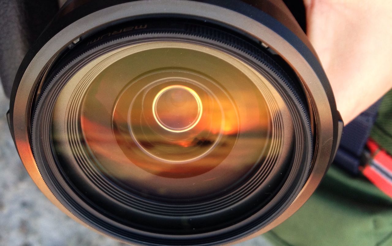 indoors, close-up, part of, focus on foreground, cropped, circle, reflection, technology, orange color, high angle view, photography themes, selective focus, camera - photographic equipment, heat - temperature, glass - material, person, detail