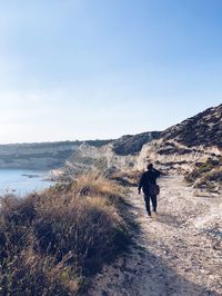 Man walking on shore by sea against clear sky