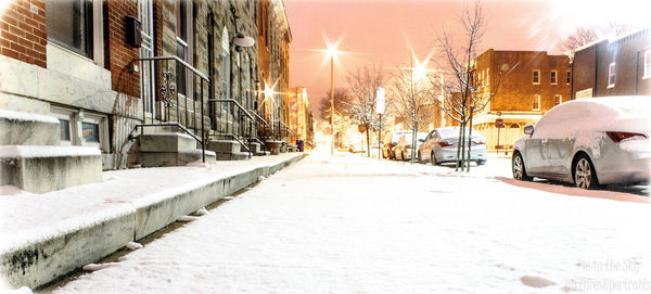 Snow covered road amidst buildings in city