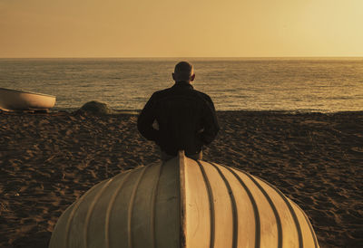 Rear view of adult man on beach with fishing boat during sunset. almeria, spain