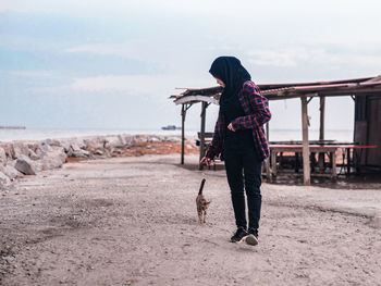 Rear view of woman walking on beach against sky