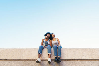 Low angle view of female friends taking selfie while sitting on retaining wall