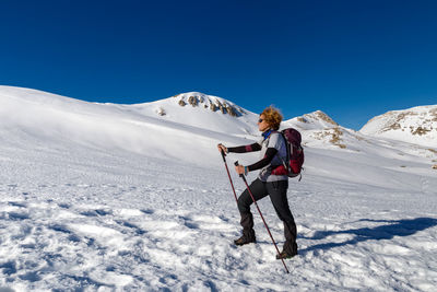 Full length of man skiing on snowcapped mountain against clear blue sky