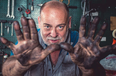Portrait of manual worker with dirty hands standing at workshop