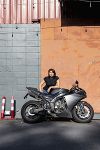 Woman leaning on her motorcycle in front of warehouse in bangkok