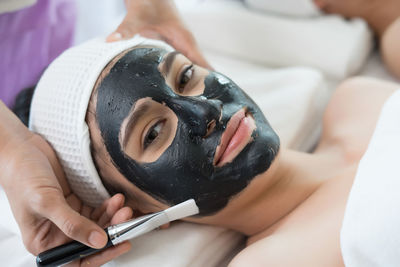 Cropped hand of massage therapist applying facial mask on young woman face in spa