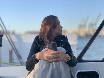 Mid adult woman holding smart phone looking through window while sitting in ship