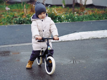 Cute toddler boy in stylish skirt riding on his balance bike at autumn park