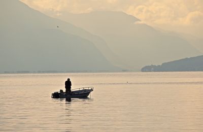 Silhouette man standing on boat moored in lake against mountains