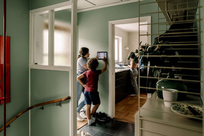 Boy using digital tablet with mother while standing near doorway at home