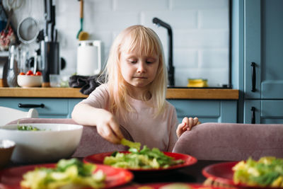 Little blonde girl is helping to prepare dinner in the kitchen.