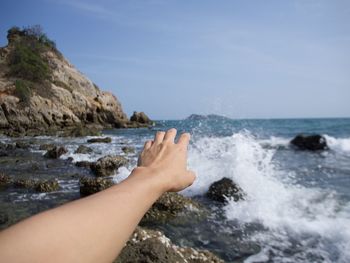 Close-up of human hand gesturing at beach against sky