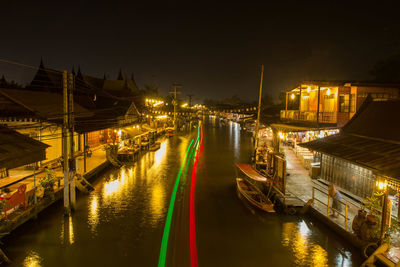 Sailboats moored on river by illuminated city against sky at night