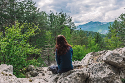 Rear view of woman sitting on rock against sky