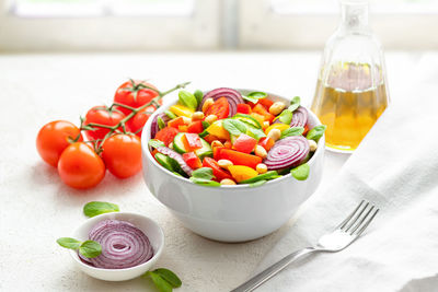 Summer salad with cherry tomatoes, cucumber, bell pepper, onion, basil and peanuts on windowsill.