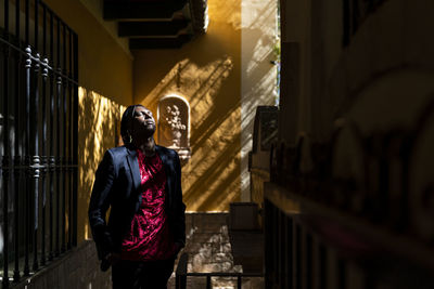 Man with eyes closed and hands in pockets standing by wall