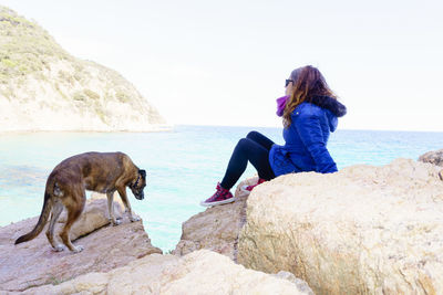 Man standing on rock by sea against sky