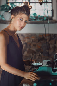 Portrait of young woman standing by typewriter and wineglass on table