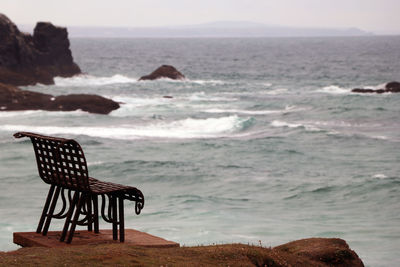 Chair on rocks by sea against sky