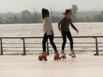 Girls roller skating on footpath against lake