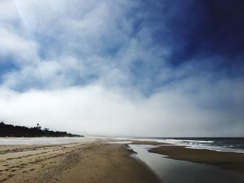 View of calm beach against cloudy sky