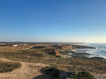 Scenic view of landscape and sea against clear blue sky