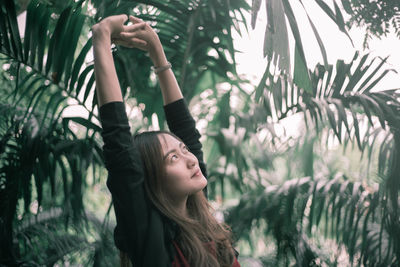 Young woman standing with arms raised against plants at park