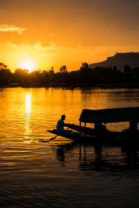 Silhouette man in lake against sky during sunset