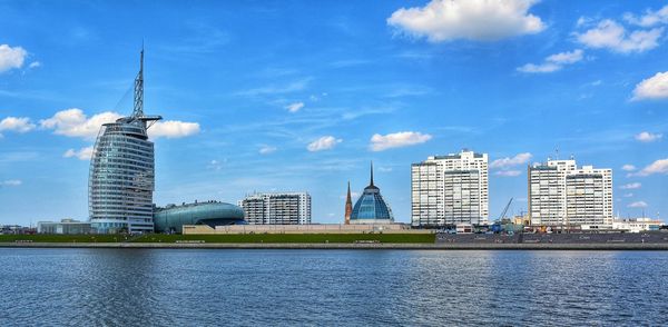 Modern buildings by river against sky in city