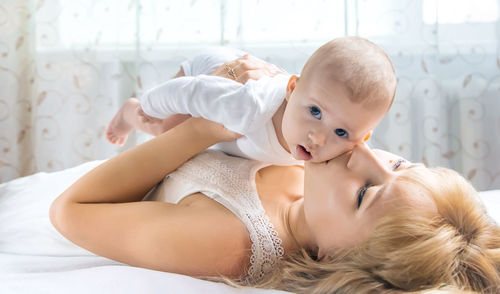 Mother kissing baby while lying on bed at home