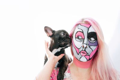 Close-up of face painted woman holding puppy against white background