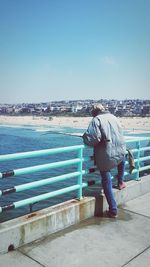 Rear view of man standing on retaining wall against sea