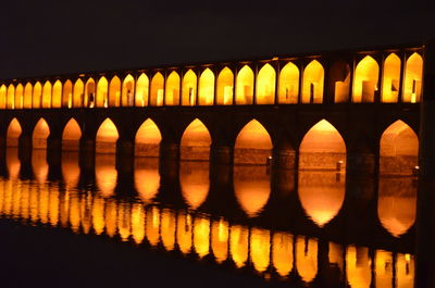 Illuminated arch bridge reflecting in river at night