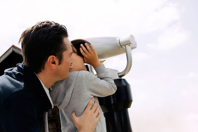 Portrait of young man holding camera against sky