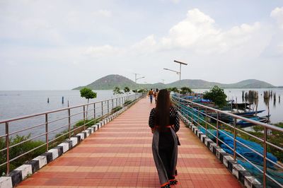 Rear view of woman on railing by sea against sky