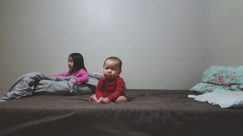 Children sitting on bed against wall