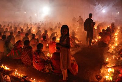 Girl looking at camera standing inside croud in rakher upobash while others are praying 